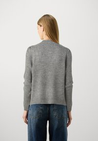 Maglione grigio lavorato a maglia con scollatura rotonda e orlo a coste. Le maniche a palloncino aggiungono dettaglio. Abbinato a jeans in denim blu a vita alta.
