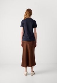 Navy short-sleeve T-shirt paired with a brown satin midi skirt, featuring a smooth texture and a relaxed fit. Casual footwear completes the look.