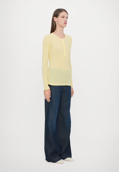 Light yellow long-sleeve shirt with a buttoned neckline, paired with wide-leg dark blue denim jeans and pointed white shoes.