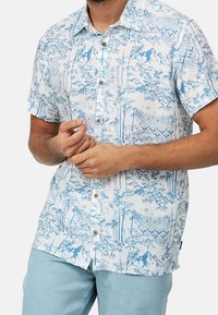 Korte mouw shirt in het wit met een blauw natuurthema print met bomen en bergen, knoopsluiting en een puntige kraag.