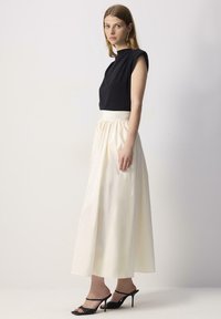 Sort cropped top med høj hals, parret med en flydende elfenbensfarvet nederdel. Nederdelen har en samlet talje og en glat tekstur. Sorte hælede sandaler.