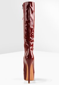 Bottes en cuir verni rouge montant au-dessus du genou, avec une finition brillante, un bout pointu et un talon stiletto haut, dotées d'une fermeture éclair latérale.