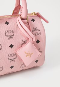 Bolso de piel rosa con logotipos impresos en negro y patrones de diamantes, una etiqueta desmontable y acentos en dorado. Acabado texturizado.