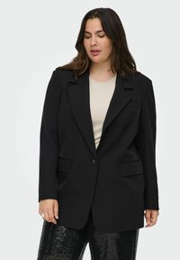 Melnas žaketes ar vienu pogu, ar izgriezumu un divām priekšējām kabatām, apvienojot ar bežīgu blūzi un melnajām biksēm ar mirdzošiem akcentiem.