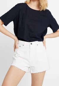Námořnická modrá lněná tričko s kulatým výstřihem a krátkými rukávy, spárované s bílými denimovými šortkami s roztrhanými okraji a pěti kapsami.