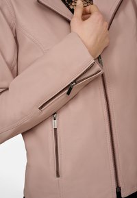 Ljusrosa läderjacka med en figurnära design, med fickor som stängs med dragkedja och metalliska detaljer på dragkedjorna.