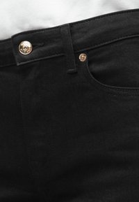 Jeans negre din denim cu detalii aurii, prezentând o închidere cu buton și o buzunar pentru monede. Textură netedă și design clasic.