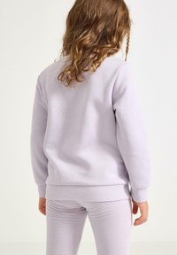 Fialová mikina vyrobená z měkké tkaniny s žebrovanými manžetami a lemem, doplněná o odpovídající fialové legíny s elegantním a jednoduchým designem.