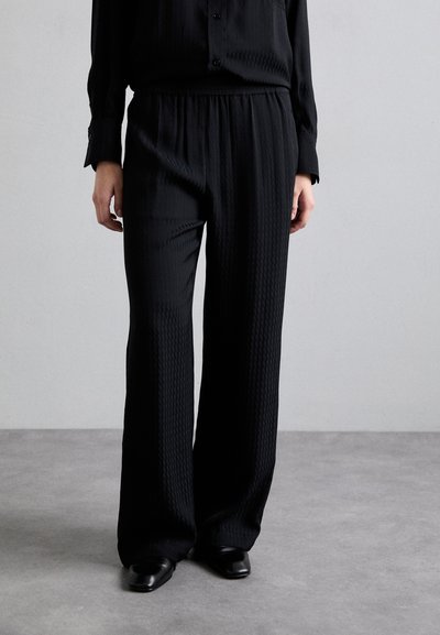 Zwarte wijde broek gemaakt van gestructureerde stof met een elastische tailleband. Gecombineerd met een bijpassend lange mouwen button-up shirt.