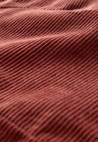 Tonfarbener Cordstoff mit auffälligem, vertikalem Rippenmuster, das eine weiche Textur und einen sanften Fall zeigt.