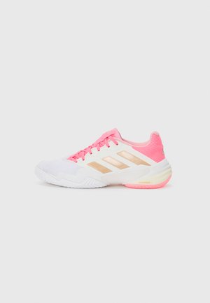 White athletic shoe with pink accents, featuring gold stripes, a textured upper, and a cushioned sole. Laces in matching pink color.