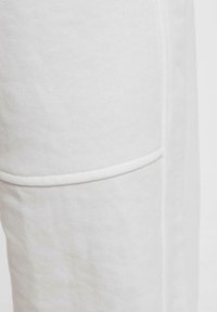 Hvide bomulds-joggers med et struktureret stof, synlig syning og en subtil, integreret lomme detalje. Glat, afslappet design.