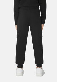 Černé cargo kalhoty s elastickým pasem, zúženými manžetami a dvěma bočními nášivkovými kapsami. Vyrobené z měkké, lehké tkaniny vhodné pro volný čas.