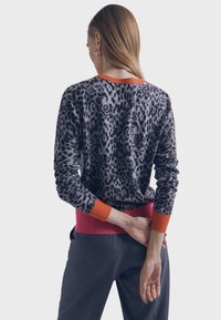 Pull imprimé léopard en gris avec bordures côtelées orange et rose. Coupe ajustée avec manches longues, texture douce et détail de couture au dos.