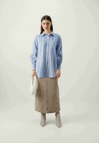 Camisa de rayas azul claro, falda midi beige, botas de tobillo grises. El conjunto incluye un bolso blanco. Enfoque en la textura de la tela y el diseño estructurado.