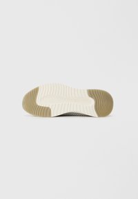 Semelle de chaussure en caoutchouc beige clair et tan, présentant des rainures et des crêtes texturées pour une meilleure traction. Motif en vagues distinctif près des bords.