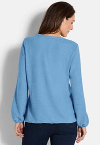 Pullover azzurro chiaro con maniche lunghe e arricciate, scollatura rotonda e vestibilità leggermente ampia, realizzato in morbido tessuto testurizzato.
