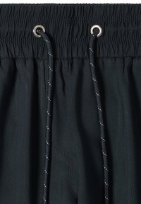 Gros plan sur un pantalon noir à taille élastique avec un cordon noir passé dans des œillets argentés à l'avant.