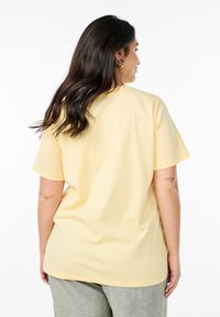 Ljusgul t-shirt med korta ärmar, rund halsringning och en avslappnad passform, tillverkad av mjukt bomullstyg. Enfärgad bakvy, utan grafik.