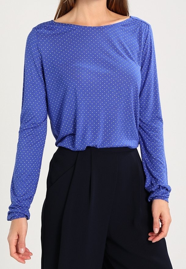 Blå långärmad skjorta med vita prickar, båturringning, mjukt tyg och avslappnad passform, i kombination med svarta högmidjade byxor.