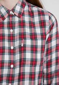 Camicia a quadri rossa, verde e bianca realizzata in tessuto intrecciato. Presenta un colletto button-down, bottoni e una tasca sul petto sinistro.