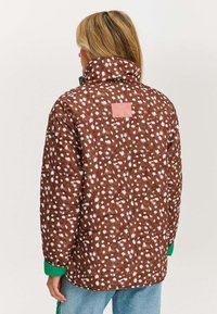 Brązowa kurtka puchowa w wzory z białymi plamkami, z wysokim kołnierzem i zielonymi mankietami. Metka z tyłu; widoczna pikowana tekstura.