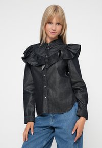 Svart denimskjorte med stor volangkrage, knappestolpe og lange ermer. Brukt med lyseblå jeans. Glatt tekstur, strukturertDesign.