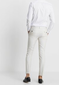 Valkoiset räätälöidyt housut, joissa on hienovarainen kiiltävä pinta, slim fit -malli ja kaksi takataskua. Yhdistetty pitkähiharaiseen valkoiseen puseroon.