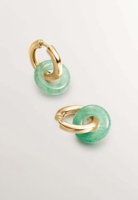 Los pendientes de aro en tono dorado presentan una piedra verde translúcida en forma de dona, que muestra una textura suave y un diseño minimalista.
