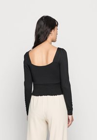 Top preto de mangas longas com decote quadrado e cintura franzida. O tecido é suave com uma textura ligeiramente elástica, apresentando detalhes em babados.