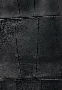 Matériau en cuir noir avec une surface texturée, comportant des panneaux cousus et un design géométrique. La finition semble lisse et mate.