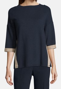 Marinblått ribbat tröja med 3/4 långa ärmar, guldglittrande detaljer vid muddar och sidor, rund krage, avslappnad passform och strukturerad tyg.