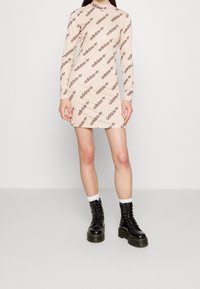 Lang roze jurkje met herhaalde zwarte "adidas"-branding, gecombineerd met zwarte veterlaarzen en witte sokken voor contrast.