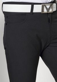 Svarta byxor i ett mjukt, stretchigt material, med ett vitt bälte med en metallspänne och två framfickor.