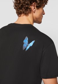 Sort bomulds T-shirt med et blåt sommerfugletryk på den øverste ryg, med klassisk rund halsudskæring og korte ærmer.