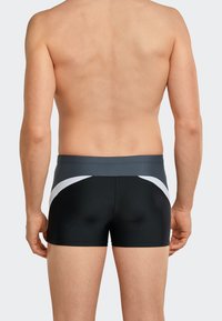 Czarne szorty kąpielowe z szarym pasem, z białymi, zakrzywionymi detalami po bokach. Gładki, elastyczny materiał dopasowuje się do ciała.