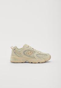 Chaussure de sport en maille beige avec des accents beiges, bout arrondi et col rembourré. Présente un logo sur le côté et une semelle texturée pour une meilleure adhérence.