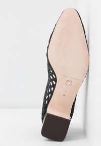 Mule tressée noire à semelle en cuir avec un talon carré, taille 8B, présentée semelle vers le haut sur un fond blanc.