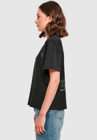 Black cotton t-shirt with a relaxed fit, short sleeves, and a white graphic design featuring "TOUR" on the back. Simple, unadorned style.