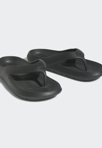 Svarta gummiflip-flops med en texturerad fotbädd, en tårem med thong-stil och subtila horisontella ränder upptill.
