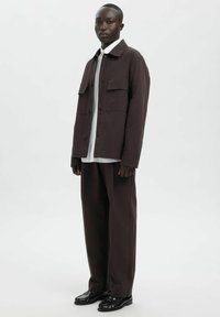 Tumepruun üle suurusega jakk kahe esitaskuga valge särgi peal, kombineeritud sobivate viimistletud pükstega ja mustade kingadega. Sile tekstuur.