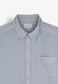 Camicia button-up grigia chiara con colletto, dotata di una piccola tasca sul petto e un logo di teschio. Realizzata in un tessuto liscio con una leggera lucentezza.