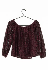 Burgundy spetstopp med långa ärmar, med ett blommönster och elastisk halsringning. Hänger från en svart metallgalge.