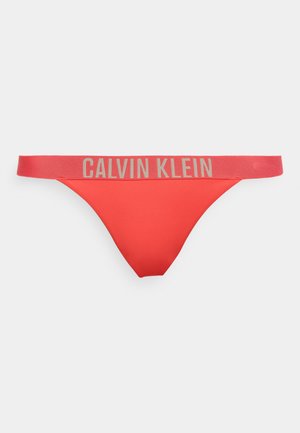 Κόκκινο γυναικείο στρινγκ με φαρδιά ελαστική μέση που έχει μεγάλο μπεζ λογότυπο Calvin Klein στο μπροστινό μέρος.
