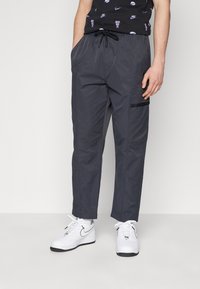 Gray lightweight cargo pants with an elastic waistband, front pockets, and a side pocket with black accent. Paired with white sneakers.