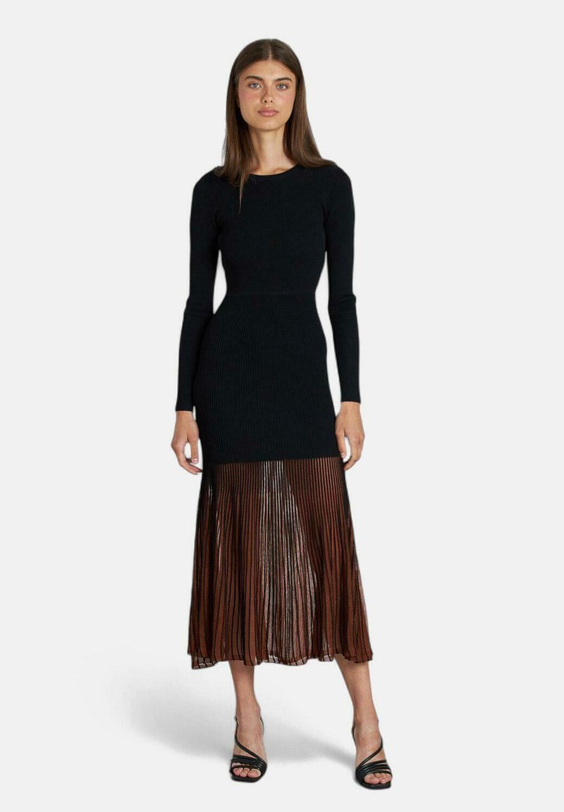 Abito lungo a maniche lunghe nero a coste con una gonna plissettata di tulle marrone. Presenta un corpino aderente e una parte inferiore fluida e texture.