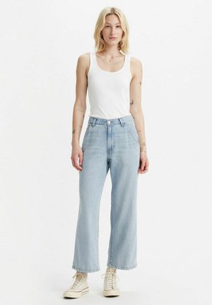 Light blue wide-leg jeans with high waist, featuring a button closure and pockets. Paired with a white tank top and beige sneakers.