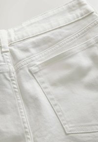 Valkoinen denimmateriaali, jossa on sileä pinta, takatasku ja hienovaraiset ompelusaumat saumoissa ja vyötäröllä.