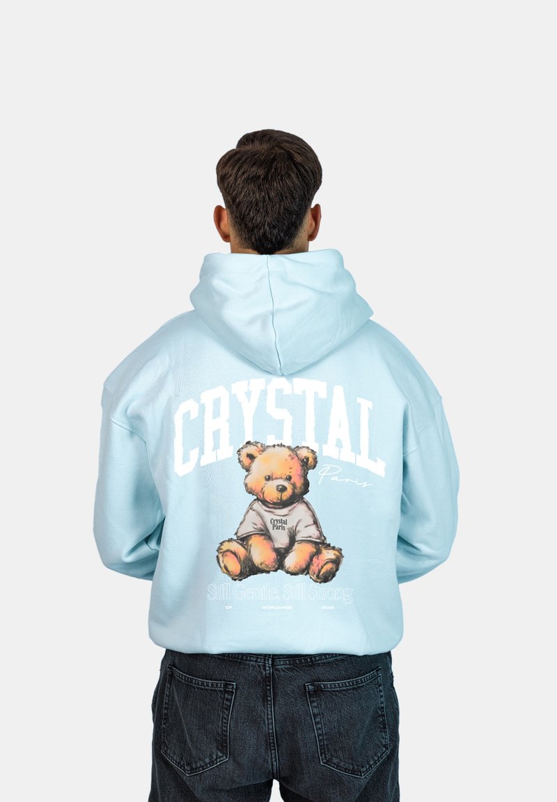 Jasnoniebieska bluza z kapturem z dużym graficznym wizerunkiem misia pluszowego i napisem 'CRYSTAL Paryż' na plecach. Miękka tkanina, przestronny kaptur i luźny krój.