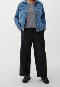 Jeansjacke in Hellblau, gestreiftes T-Shirt mit Rundhalsausschnitt, dunkle weite Hosen und schwarze Plateauschuhe. Mit Metallknopf-Akzenten.